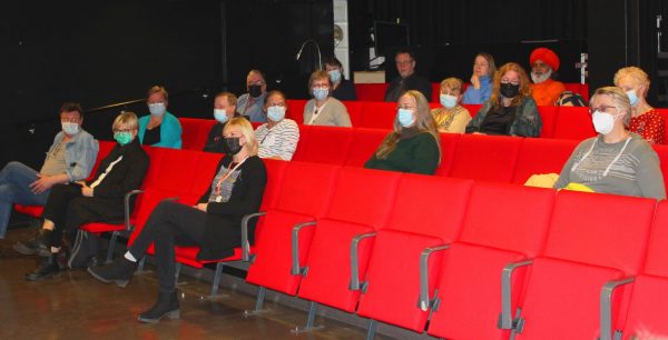 Yleisöä auditoriossa, oranssit penkint kuuntelee paneelikeskustelua